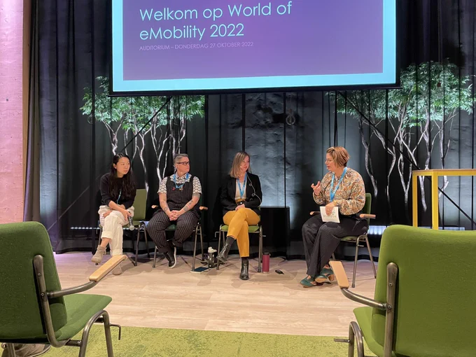 Four people sit down at a panel on green chairs in a podium