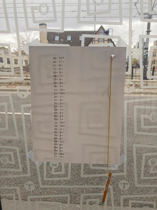 A subtraction worksheet is taped to the inside of a bus shelter, together with a golf pencil on a string. The worksheet is untouched.