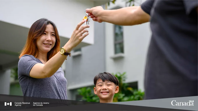A parent and their child smile as someone hands them a set of house keys.