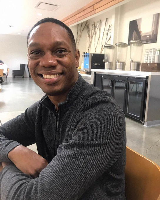 Jerry smiling inside of a room, with his face turned to the left, wearing a gray sweater.