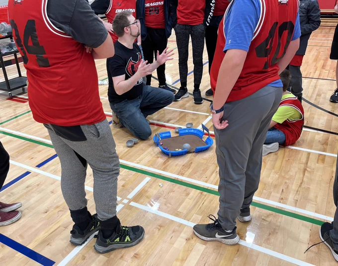 Teacher on floor with students watching game demo from above .