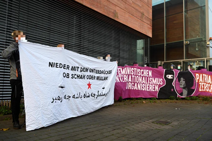 Aktivist*innen vor dem Konsulat der Islamischen Republik Iran. Aufschrift der Banner: "Nieder mit dem Unterdrücker, ob Schah oder Mullah!" und "Feministischen Internationalismus organisieren"