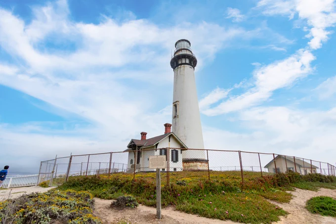 Pigeon Point Lighthouse reaches up towards a bright, lightly cloudy blue sky