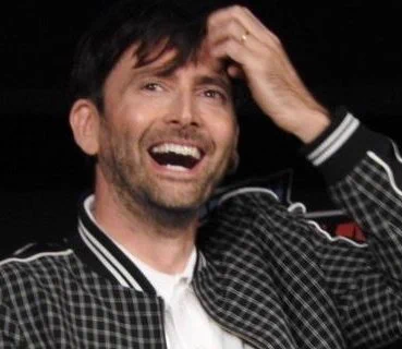 David Tennant looking up with a huge smile on his face. You can hear his laugh through the photo. 