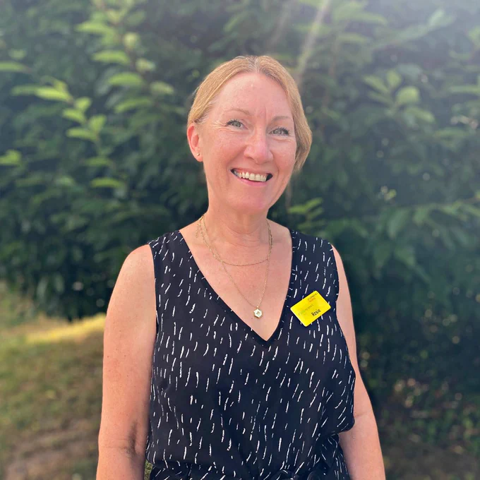 Rosie, wearing a black spotted blouse and yellow name badge, smiling at the camera.