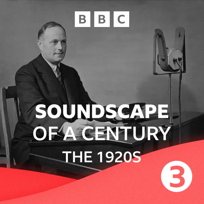 Man in suit sits in front of a microphone with a script in the 1920s.