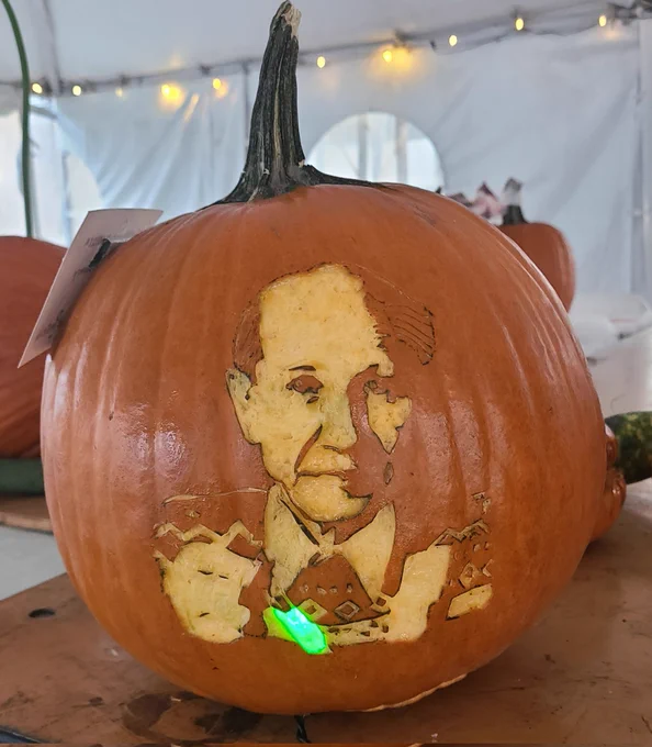 Portrait of Osamu Shimomura (1/3 of the Nobel Prize in Chemistry 2008) carved in relief onto the surface of a pumpkin. In his hand is a vial which has a green bulb sticking out of it to resemble the glow of isolated Green Fluorescent Protein (GFP).