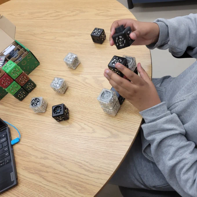 Hands holding cubelet blocks to stack together on a brown table 