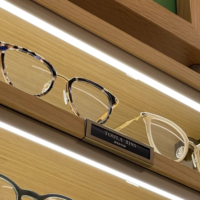 Eyeglasses on a shelf labeled “Toula”.