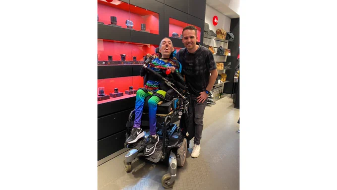IMAGE DESCRIPTION 3: Portrait photo of Sulaiman and Will in front of a display of cameras and camera accessories at Leica Store Mayfair. Both are smiling and are joyful.
