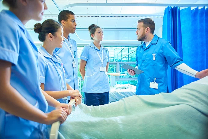 A group of nurses is instructed by a nurse educator on a hospital ward.
