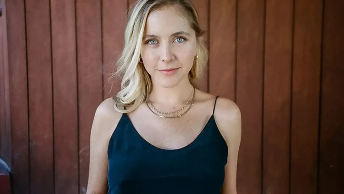Photo of Stephanie Danler smiling at the camera. She is in front of a wood slatted wall. Photo credit: Emily Knecht