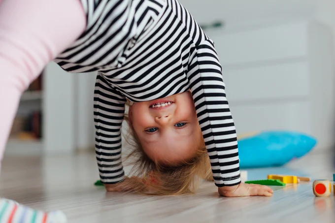 A happy toddler turning herself upside down and smiling at the camera.