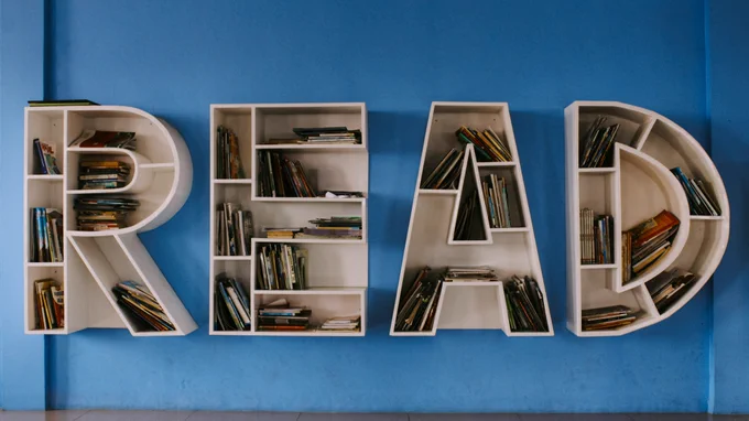 Photo by Ishaq Robin on Unsplash shows white bookshelves in the shape of the letters R-E-A-D on a blue background