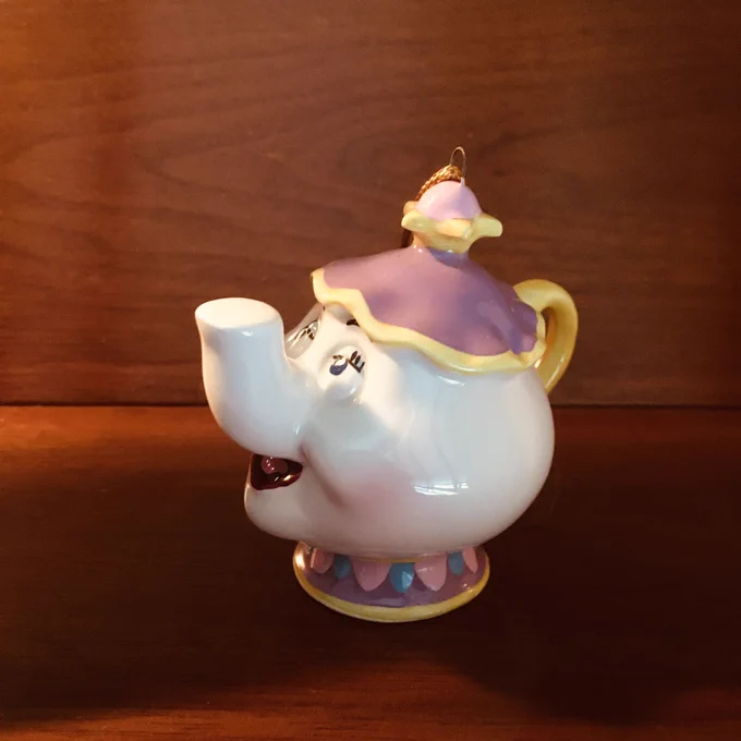 A small figurine of Mrs. Potts sits on a wooden shelf.