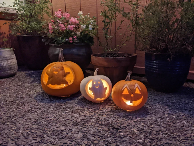Three carved Halloween pumpkins sit on a stoop. There's a classic jack o' lantern and two ghosts. One of the ghosts is cute and smiley, and another looks more vengeful.