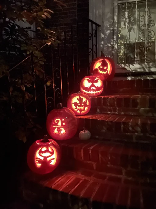 Five jack o’lanterns in a row, one on each step. They are glowing by candlelight