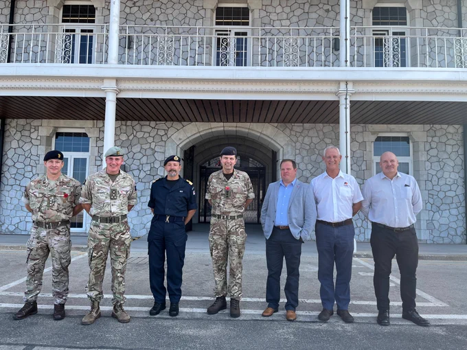 A group photo showing Brigadier Jonathan Bartholomew, DIO's Head of Overseas and Training Region alongside Commodore Tom Guy, Commander British Forces; Adrian Stevens, Mitie Defence Sector Director, and other DIO and Mitie representatives. The four men on the left are in military uniforms, with the three other individuals wearing civilian attire. 