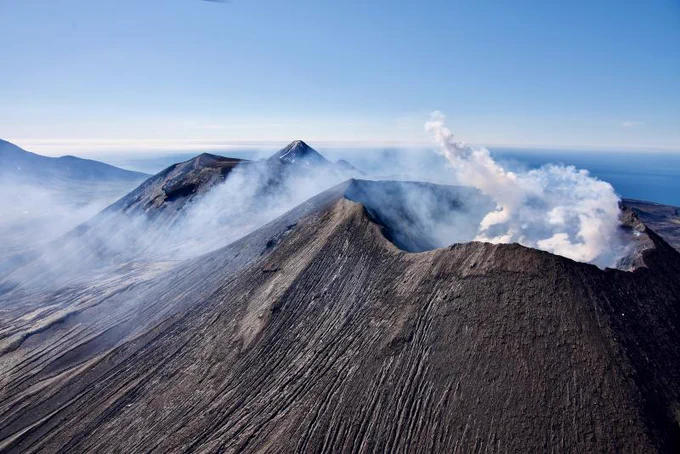 Peak of a volcano with white gas plumes rising out of the crater.