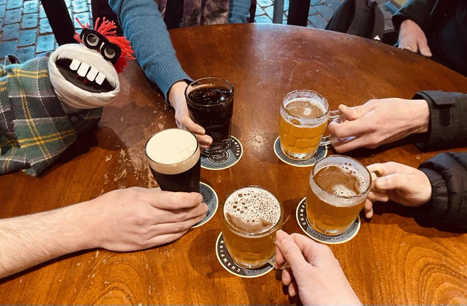 Hands with beers cheersing with sock puppet archivist hanging out with the humans, loving life