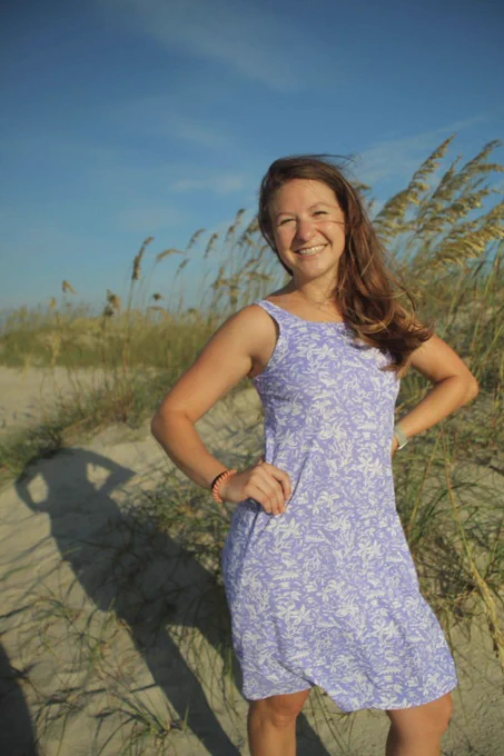 Anna Atencio stands on the beach with dunes behind her.