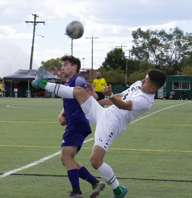 Two soccer players appear to collide while one tries to kick the ball and another attempts to head the ball. 