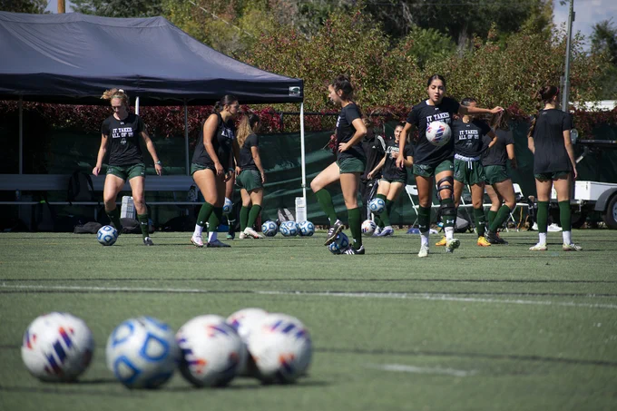 Soccer balls are in the foreground as soccer players warm up on the field. 