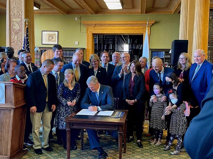 A picture of Governor Charlie Baker signing the Inclusive Concurrent Enrollment law around legislators and advocates. 