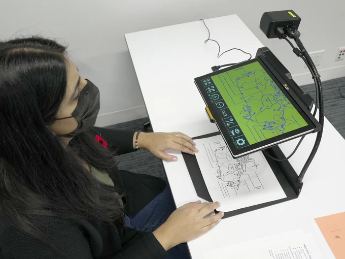 Woman working on the MagniLink TAB by Lvi Low Vision International. Screen shows a magnified map with green background.