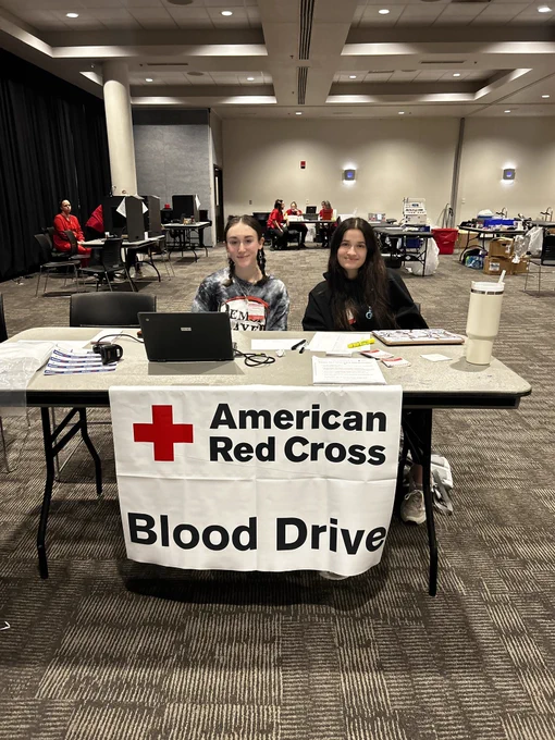 Two students sitting at a check in table for the “American Red Cross Blood Drive” in Skutt Ballroom