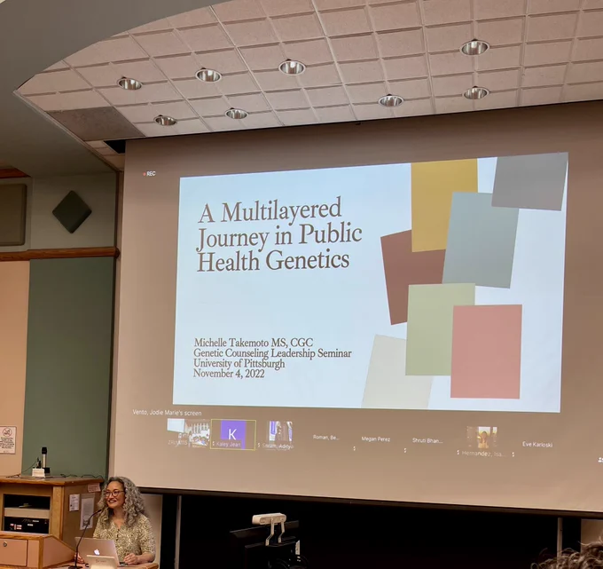 Michelle Takemoto standing in front of podium giving a guest lecture titled "A Multilayered Journey in Public Health Genetics" at the University of Pittsburgh.