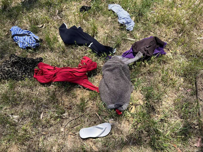 A jumble of abandoned clothes and white thong (flip flop) on a dappled, unmowed, early summer lawn