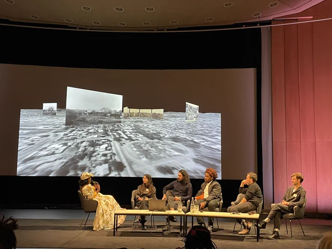 Im Hinterhrund: Still aus Film von Forensic Architectur. Im Vordergrund: Podium - Kambanda Veii, Ashkan Cheheltan, Tobechukwu Onwukeme, Agata Nguyen Chuong, Eyal Weizman