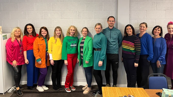A group of people wearing colourful clothes to make a rainbow.