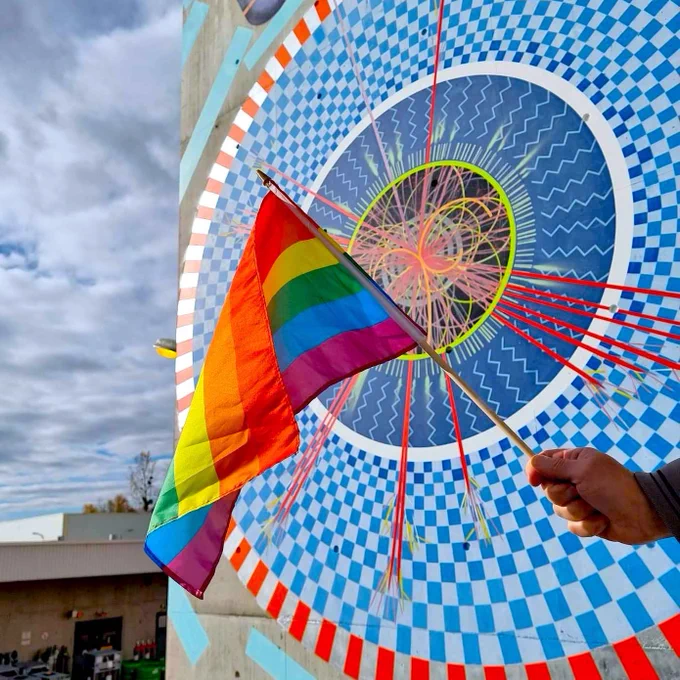 Pride flag held outside, in front of the ATLAS Mural.
