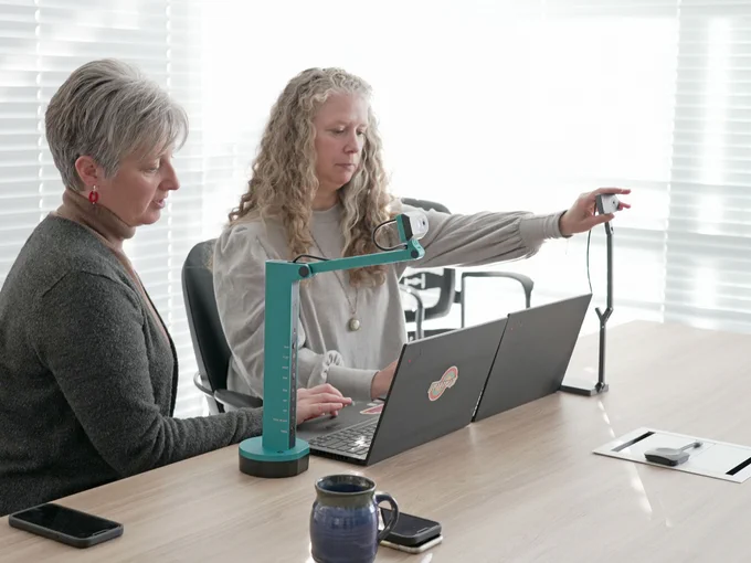 Kim and Naomi sitting at table testing a document camera.