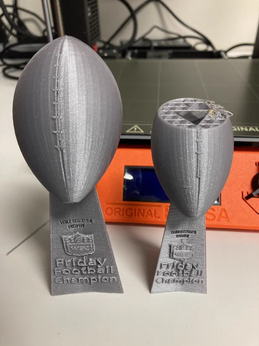 Two 3d printed Lombardi trophies with the words, Friday football champions”. One is five inches tall and another three inches tall. The three inches tall trophy print failed near the top of the football. You see the inside of the trophy, which has diagonals.
