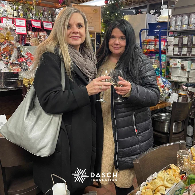 Two attendees smile at the camera and clink their wine glasses.