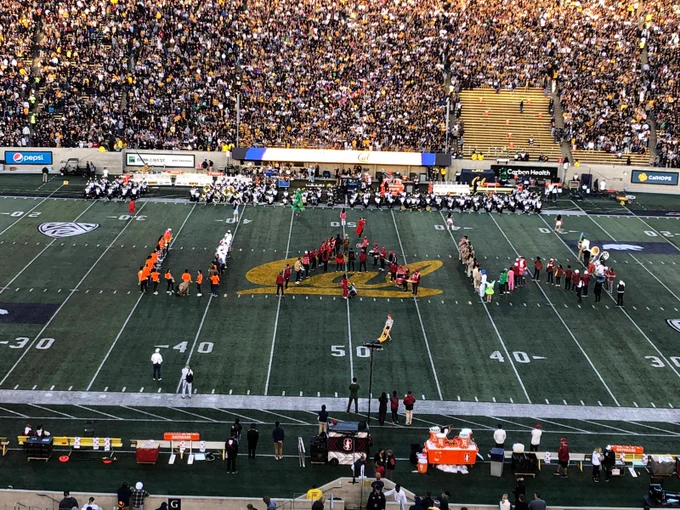 A photo of the Cal football field with Stanford band members forming the letters UAW with their bodies on the field. Behind them is a giant crowd in the stadium. They are wearing many colors. 