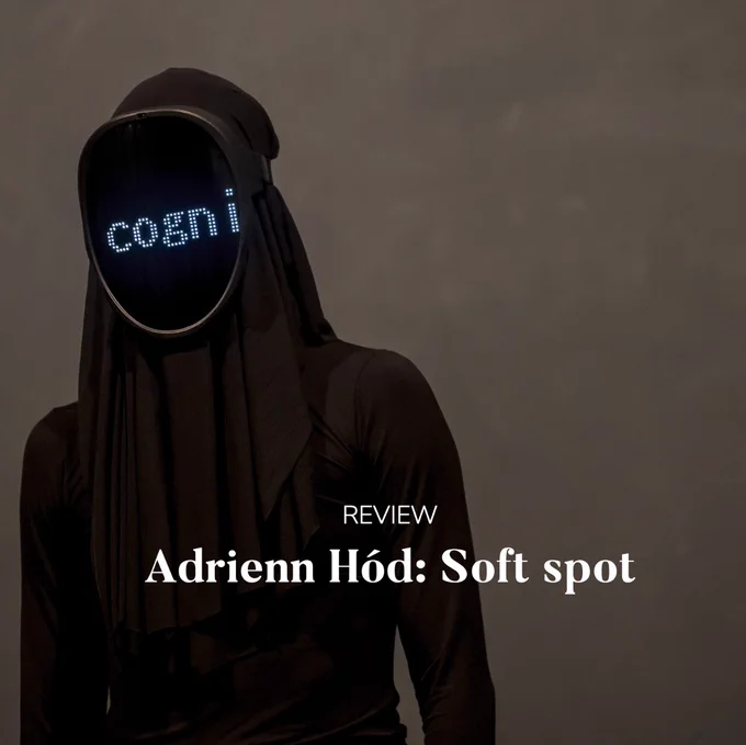 Photo of a figure dressed all in black with face covered by screen which says 'cogni'. Title 'Review: Adrienn Hód: Soft spot' on top.
