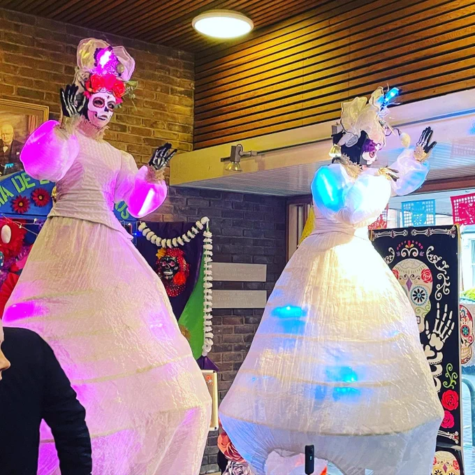 Las muertas stilt walkers in white dress with large crinoline and blue and purple lights.