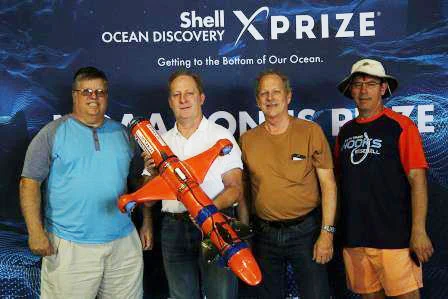 Photo of Ed Larson, Dennis Lorence, Joe Daum, and Terry Meier standing on a stage holding an underwater explorer with XPRIZE in background.