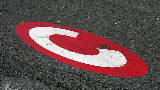 London’s Congestion Charge roundel - a white C inside a red circle – painted onto on a grey tarmac background.