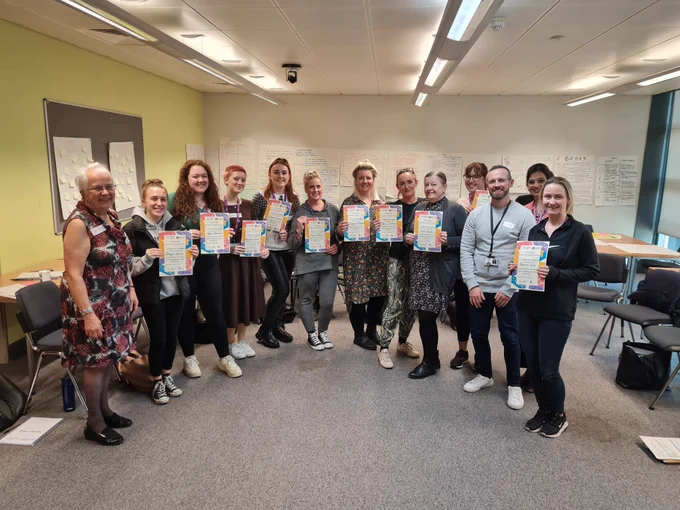 Students, lecturers and trainer holding certificates in a classroom 