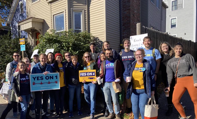 Big group of smiling canvassers in front of a house in Somerville, holding signs that say YES ON 1 and YES ON 4.