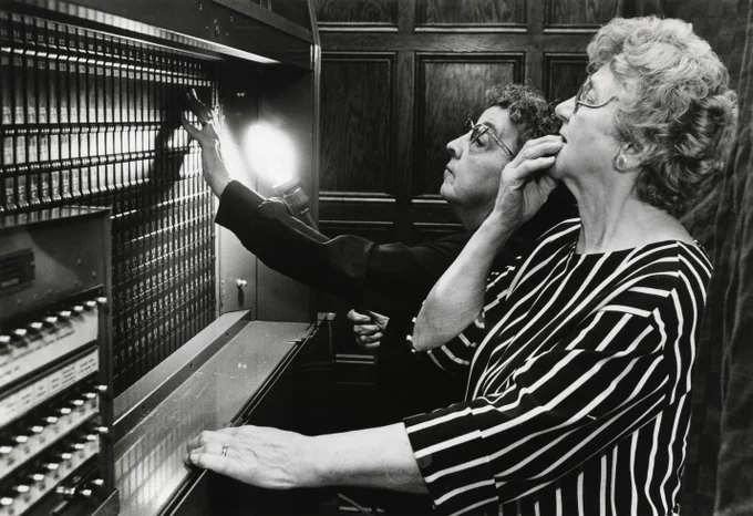 Two women standing at the back of a voting machine, with looks of concentration.