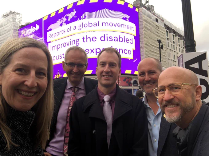 Five Disability and Access Ambassadors in front of the Purple Tuesday billboard at Piccadilly Circus, London. Left to right is Kathryn Townsend DAA for banking, Peter Hamilton DAA for insurance, Ross Calladine DAA for tourism, Ben Horner DAA for retail, and Hector Minto DAA for technology.