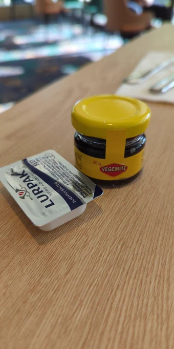 A single use disposable butter pack next to a 20g jar of Vegemite 