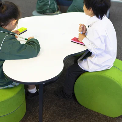 2 students sitting on Rockable ottomans in different ways, using a writable Cloud table