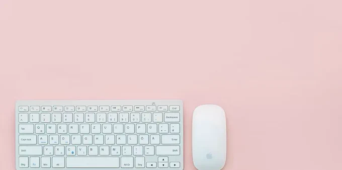 A photo of a white mouse and keyboard on a pink background.